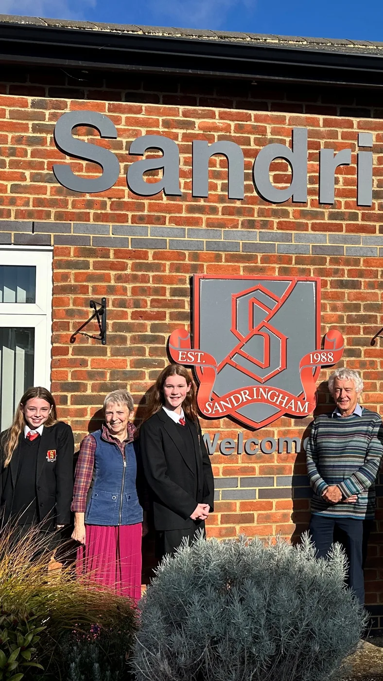 Two Year 7 pupils in school uniform stand with Councillors Allison Wren and Anthony Rowlands below the Sandringham School sign.