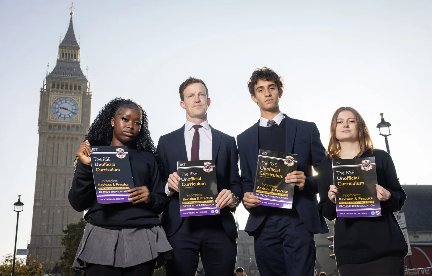 Alistair Strathern MP stands with three young people in school uniform, each holding a copy of the RSE Unofficial Curriculum, with the Elizabeth Tower behind them