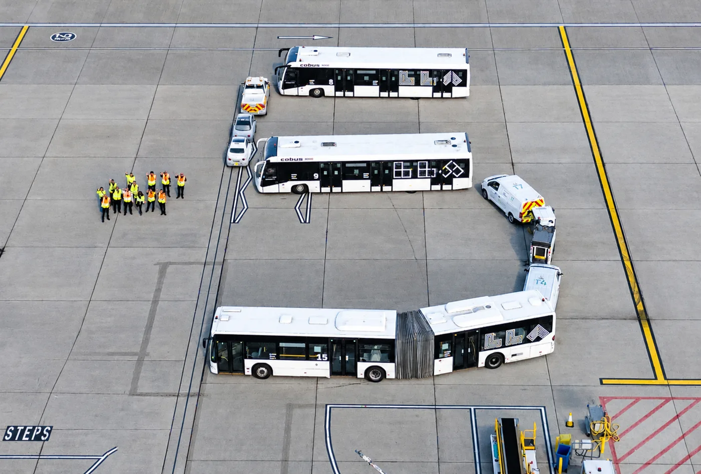 Airport buses, vans and cars lined up in the shape of a number 5 on the apron at London Luton Airport, with staff in hi-vis standing alongside