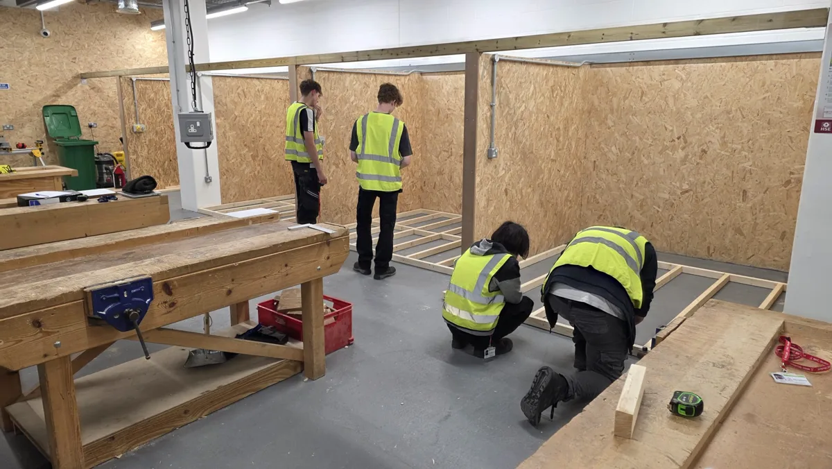 Four students in hi-vis vests working on timber in a carpentry workshop with plywood booths at North Hertfordshire College's Town Centre Campus